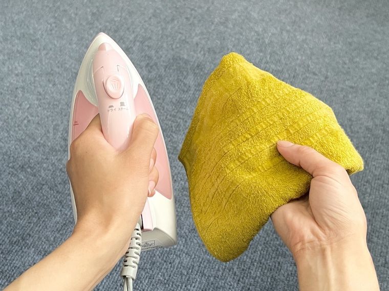 アイロンと湿らせたタオルを両手で持っている様子