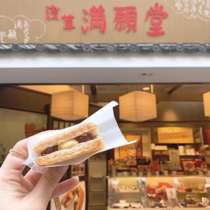 お店の看板を背景に店舗限定の芋くりパイを手に持っている様子