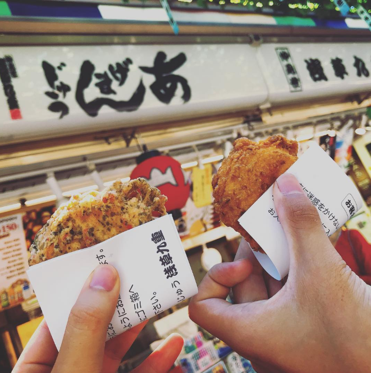 浅草九重の店頭でふたつのあげまんじゅうを手に持ち掲げている