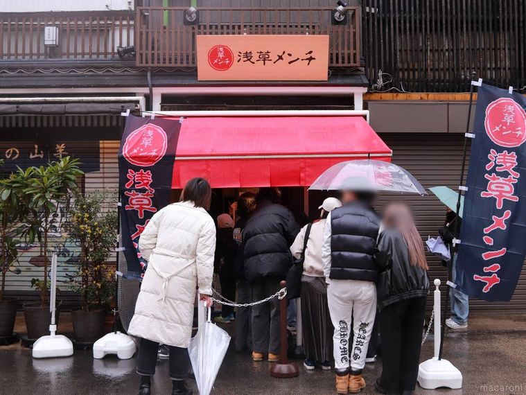 雨天のなか、傘をさす人で行列ができている浅草メンチの外観
