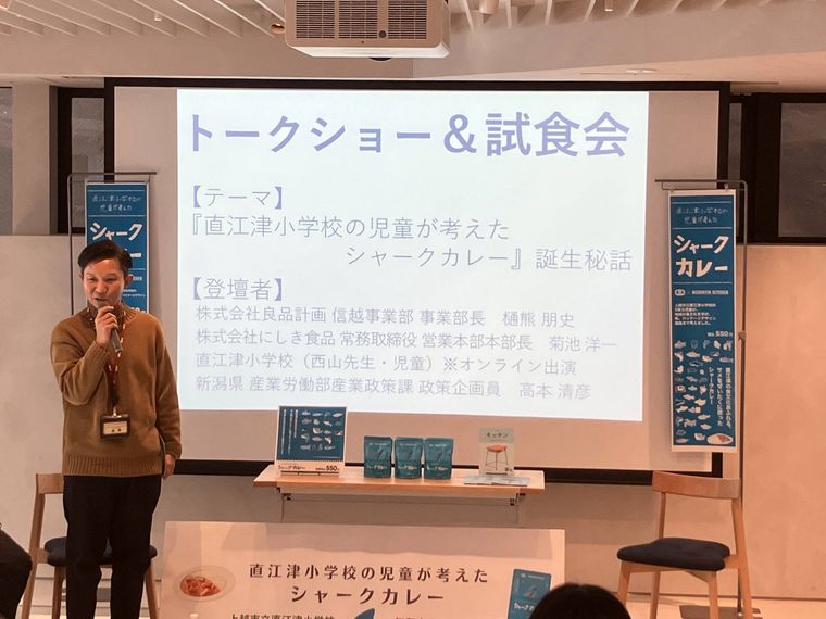 スクリーンの前でシャークカレーの誕生秘話を話す男性