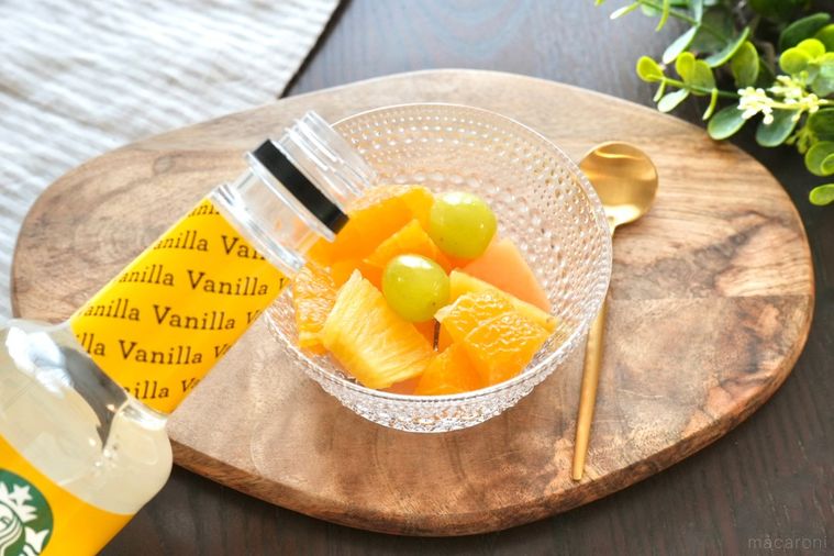 木のカッティングボードにのったガラスの器に盛られたフルーツカクテルと金のスプーンとストライプの布