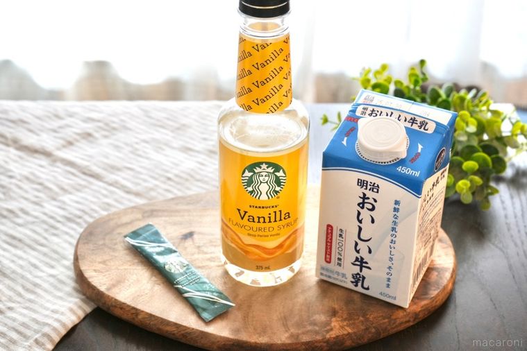 木のカッティングボードにのったインスタントコーヒーとバニラシロップと牛乳とグリーンとストライプの布