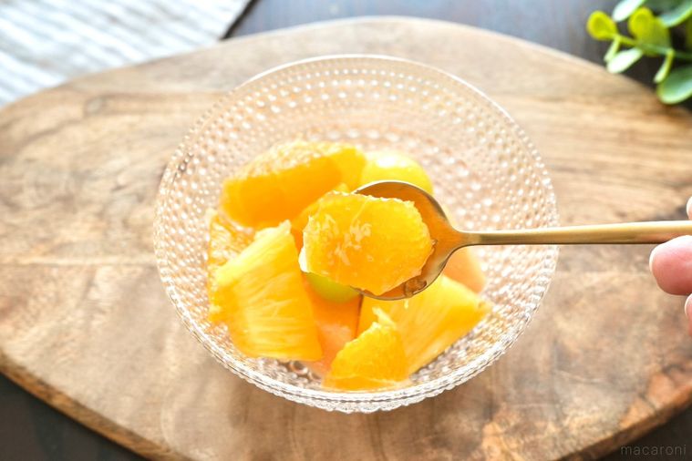 木のカッティングボードにのったガラスの器に盛られたフルーツカクテルと金のスプーン