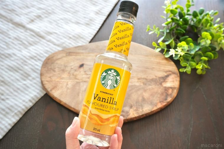 木のカッティングボードと手に持った黄色いボトルのバニラフレーバーシロップとグリーンとストライプの布