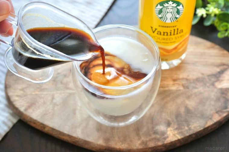 木のカッティングボードにのったグラスに牛乳とコーヒーを注ぐ様子