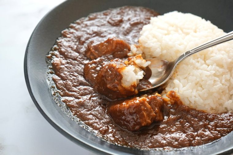 大理石の背景と黒い器に盛られた空港ラウンジのカレーライスをシルバーのスプーンで食べる様子