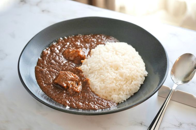 大理石の背景と黒い器に盛られた空港ラウンジのカレーライスとシルバーのスプーン