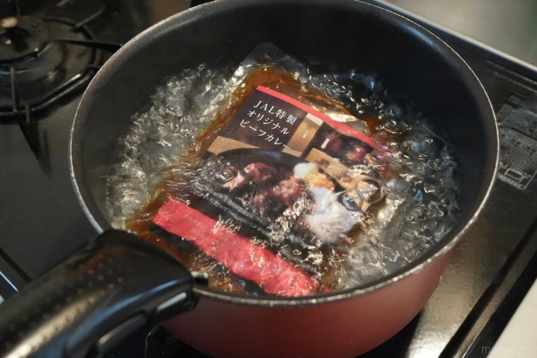 赤色と黒色の鍋でカレーのパックを湯煎解凍する様子
