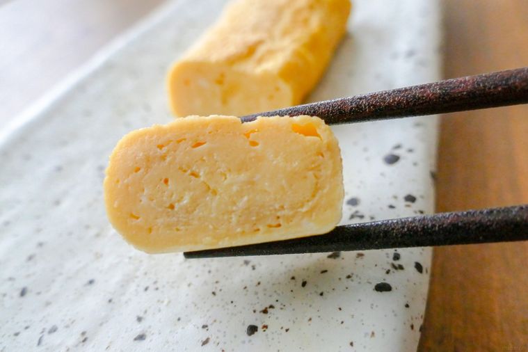 卵焼きひと切れを箸で持ち上げる様子
