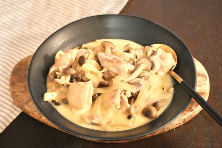 黒い器に盛られたチーズクリームチキンソテーと金のスプーンとストライプの布