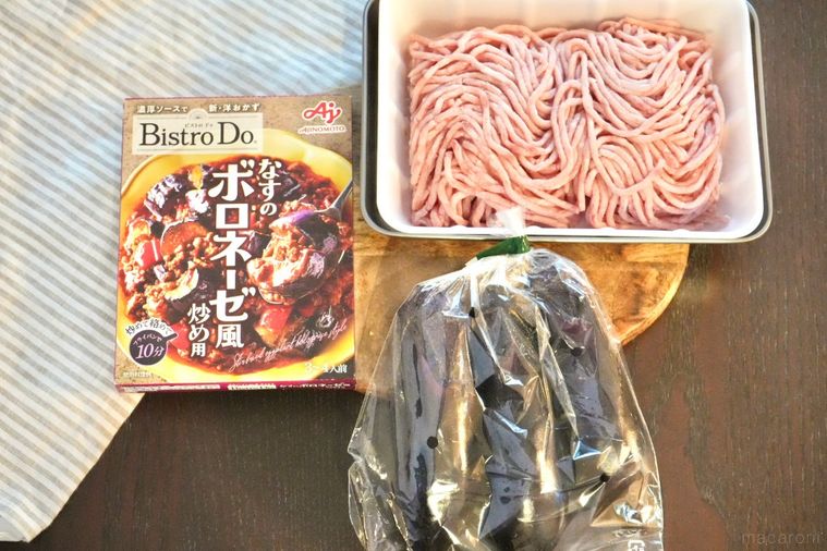 木のカッティングボードにのったなすと挽肉とボロネーゼ風のソースとストライプの布