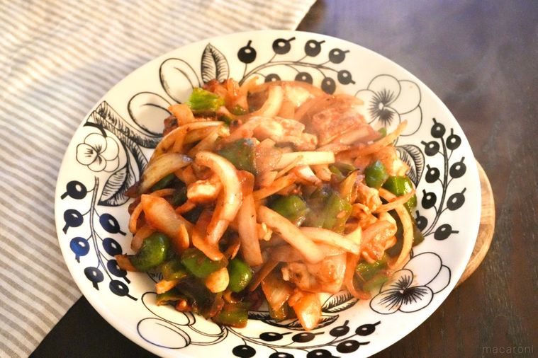 白い大皿に盛られた鶏肉とピーマンと玉ねぎのトマトソースソテーとストライプの布