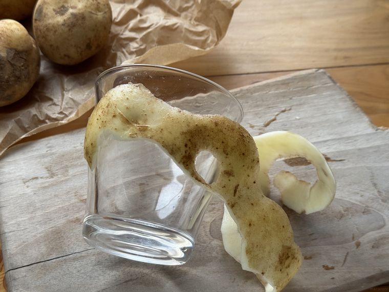 木のカッティングボードの上に横になったガラスコップとじゃがいもの皮