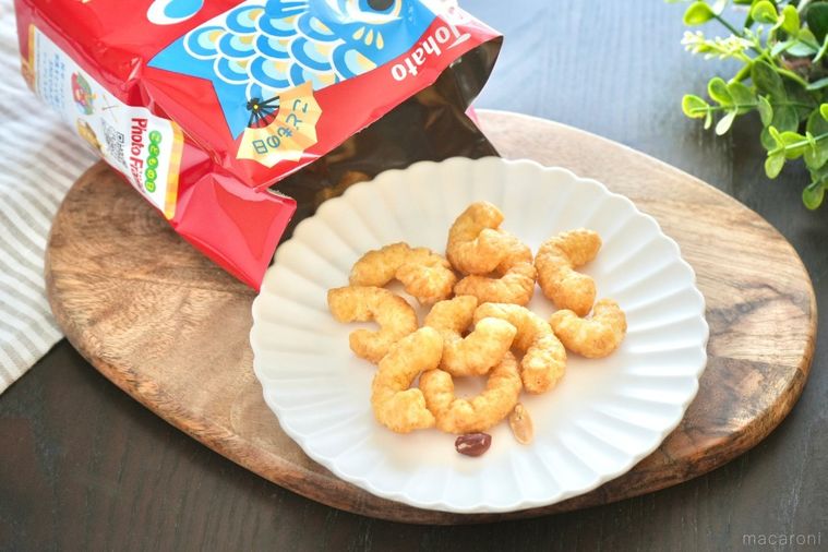 木のカッティングボードと白い皿にのった赤いパッケージのキャラメルコーンとストライプの布とグリーン