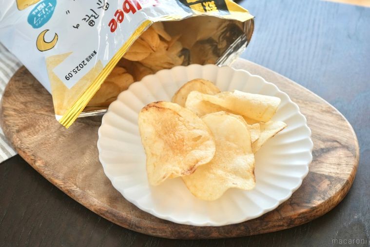 木のカッティングボードと白い皿にのったトリュフ塩味ポテトチップスのパッケージの袋とストライプの布