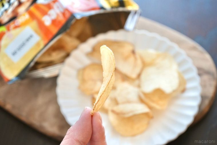 木のカッティングボードと白い皿にのった唐揚げ味のポテトチップスを手に持つ様子とパッケージの袋