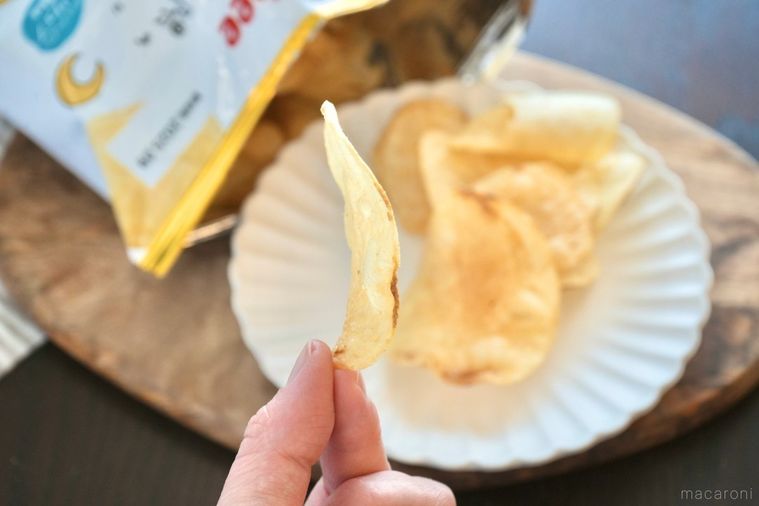 木のカッティングボードと白い皿にのったトリュフ塩味ポテトチップスを手に持つ様子とパッケージの金色の袋