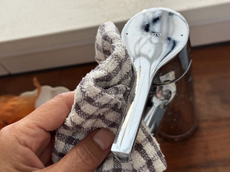 左手に持ったチェックのふきんでステンレス製蛇口を拭いている様子