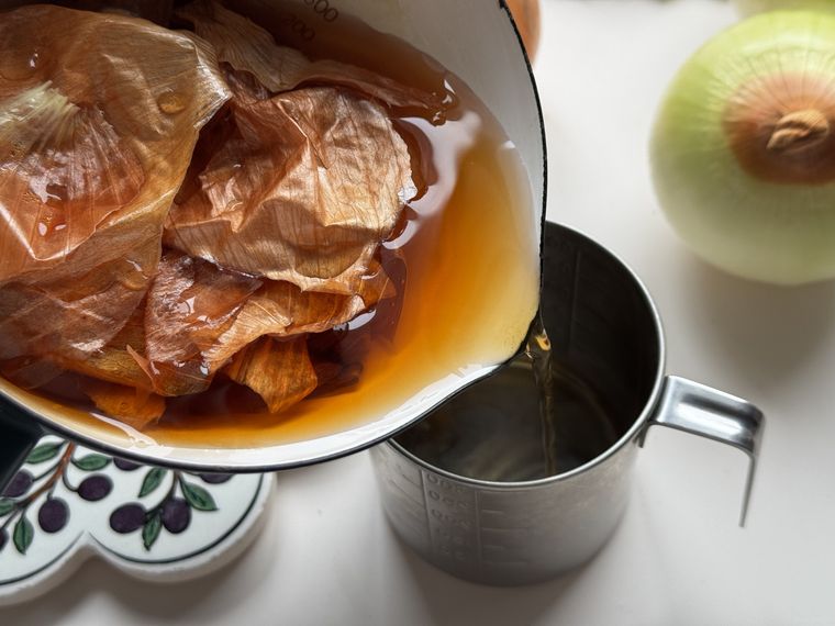 玉ねぎの皮と煮汁の入ったホーロー小鍋を傾けて、煮汁を計量カップに移している様子