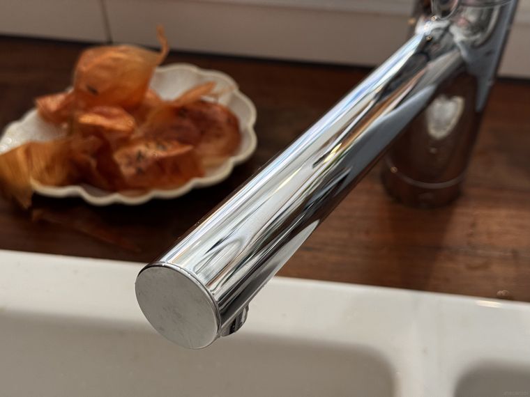 直線型のステンレス蛇口と白い陶器のシンク、木のキッチントップに皿に入った玉ねぎの皮が置かれている様子