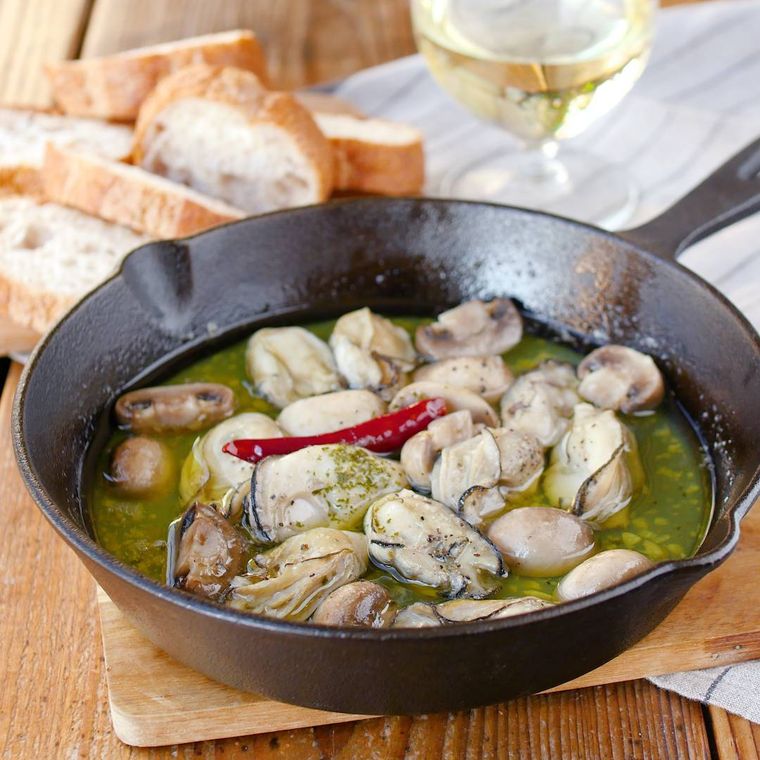 スキレットに入っている牡蠣のアヒージョがある食卓