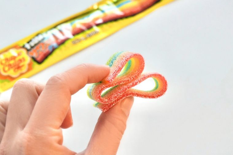 白い背景とカラフルなレインボーグミを折りたたんで手に持つ様子