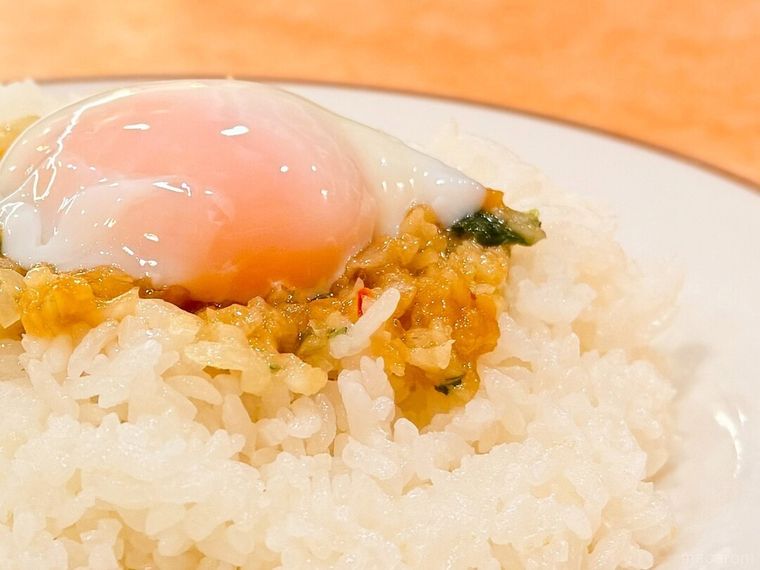 ご飯の上に半熟卵やソースを盛り付けている様子