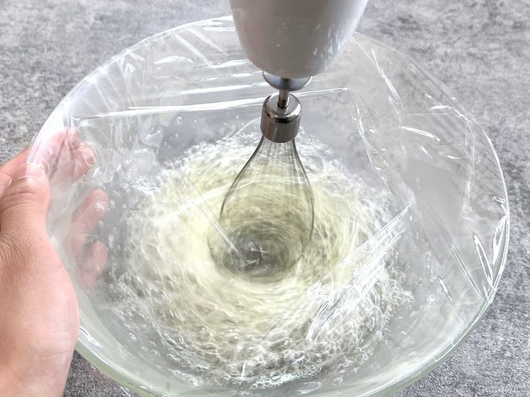 ラップをかけたボウルで卵白を泡だてている様子