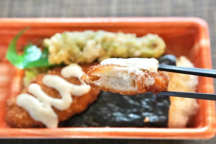 茶色いランチョンマットとちくわ天がのったのり弁当の白身魚のフライを黒い箸で持ち上げる様子