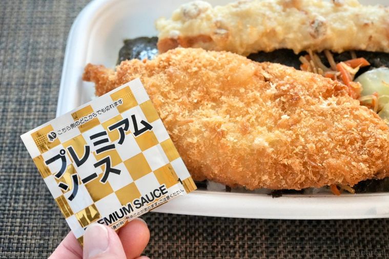 白身魚のフライがのったのり弁当とソースの袋を持つ手