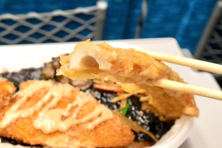 白いトレーの白身魚のフライときんぴらごぼうとしば漬けがのったのり弁当のちくわ天を割り箸で持ち上げる様子