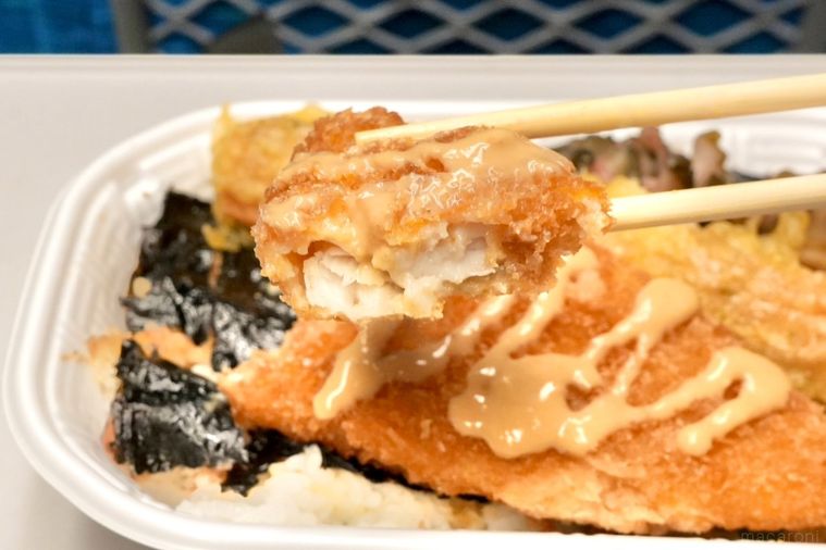 白いトレーのちくわ天ときんぴらごぼうとしば漬けがのったのり弁当の白身魚のフライを割り箸で持ち上げる様子