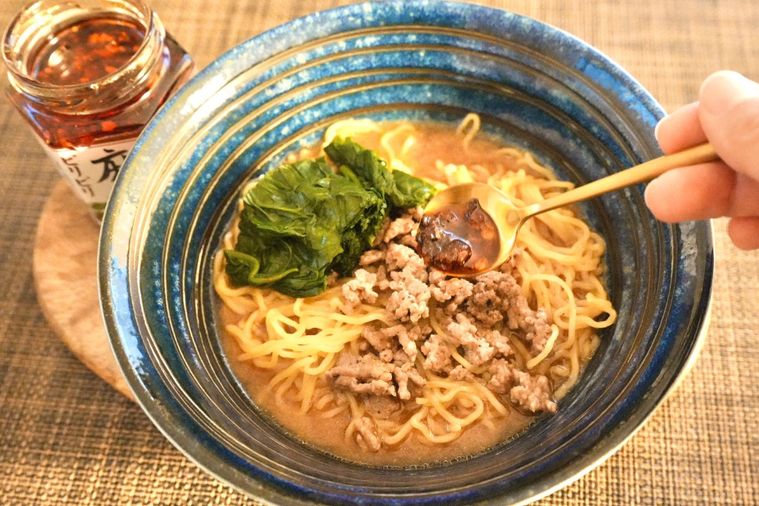 ほうれん草がのった味噌坦々麺に麻辣醤を金のスプーンでかける様子と青い器