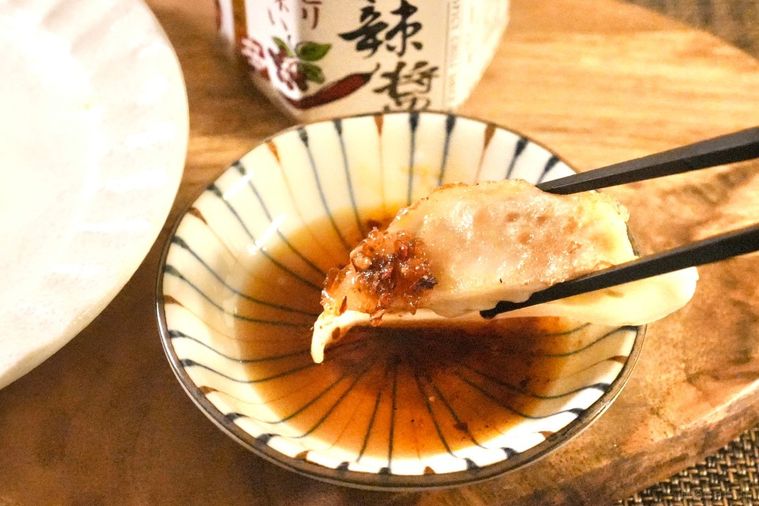 木のカッティングボードにのったたれの入った小皿に餃子をつけて食べる様子