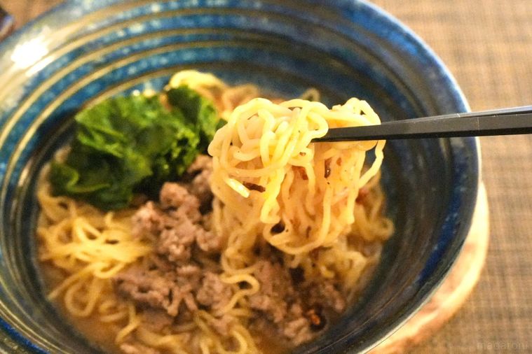 青い器に盛られた坦々麺を黒い箸で食べる様子