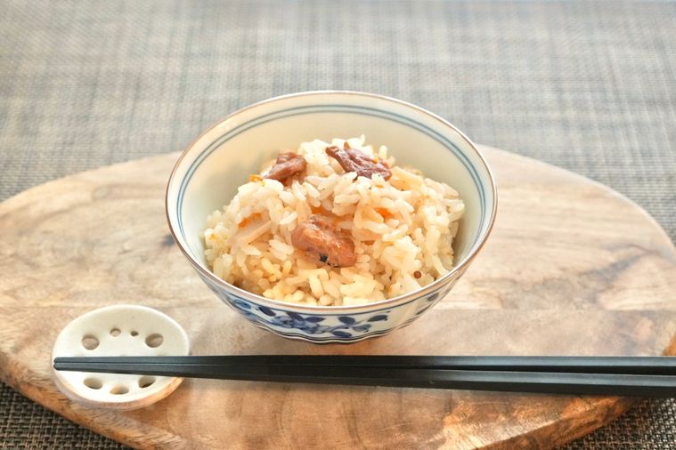 木のカッティングボードにのった茶碗に入ったたこめしと黒い箸