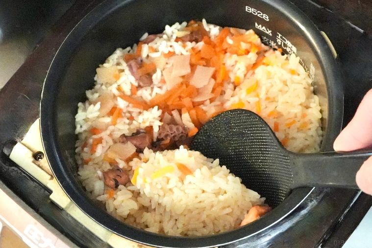 炊飯器に炊き上がったたこめしを黒いしゃもじで混ぜる様子
