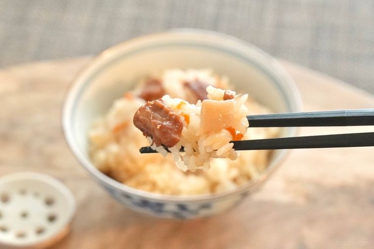 木のカッティングボードにのったごはん茶碗に盛られたたこめしを黒い箸で持ち上げる様子