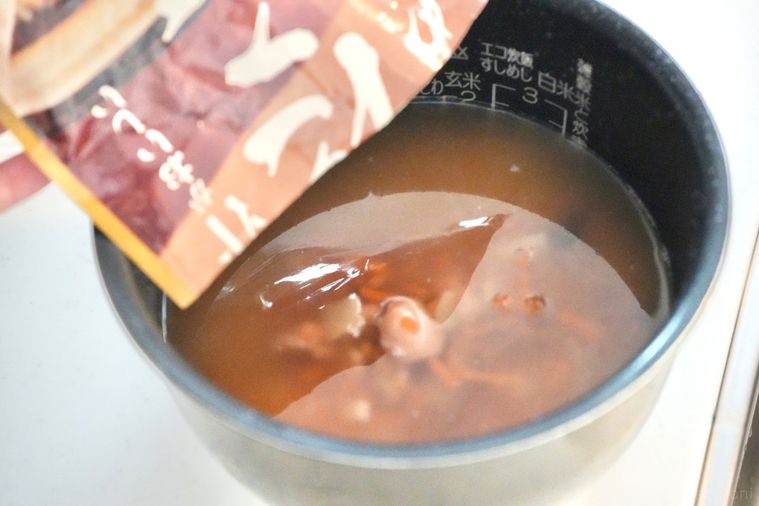 炊飯器に入った研いだ米とたこめしの素を入れる様子