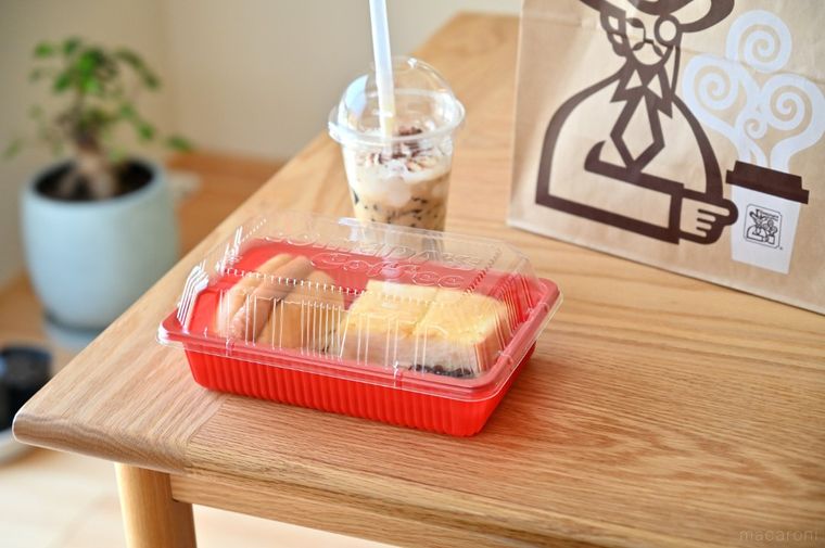 木のテーブルに置かれたコメダのテイクアウト料理とドリンク