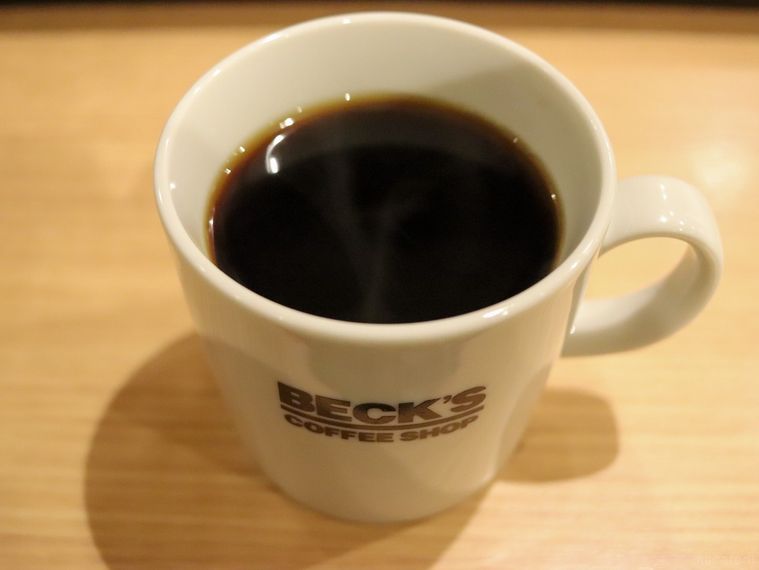 木製のテーブルの上にベックスの白いオリジナルカップに入ったブレンドコーヒーが置かれている