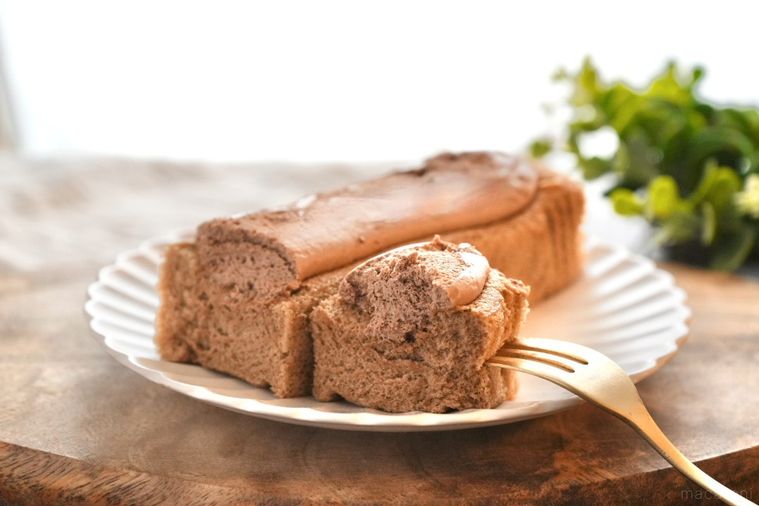 木のカッティングボードと白い皿にのったショコラクリームのせ生シフォンを金のフォークで食べる様子