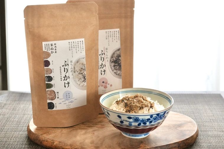 茶色いテーブルクロスと木のカッティングボードにのったごはん茶碗と米ぬかふりかけの茶色い袋2つ