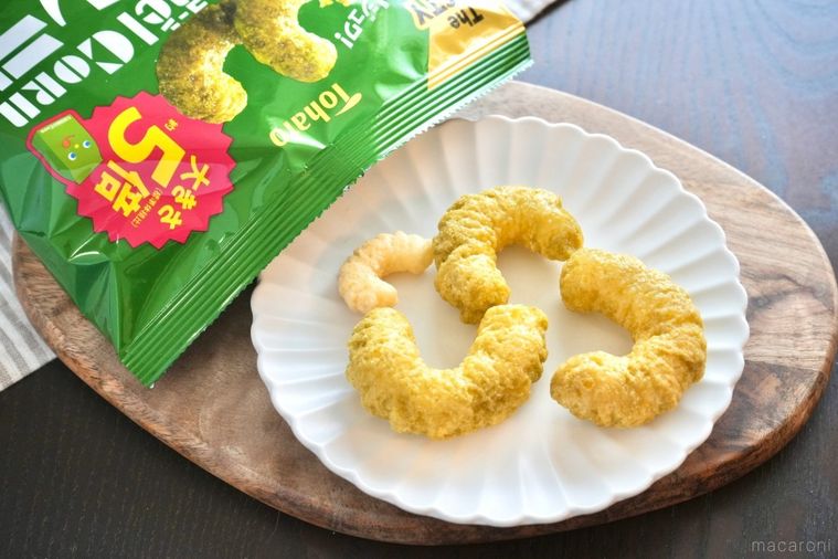 木のカッティングボードと白い皿にのったキャラメルコーングランデと緑色の袋のパッケージとストライプの布