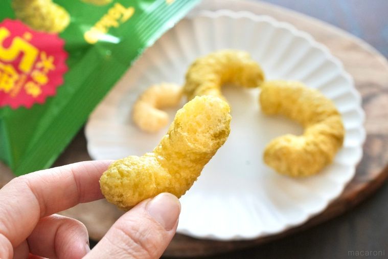 木のカッティングボードと白い皿にのったキャラメルコーングランデを持つ手と緑色の袋のパッケージ