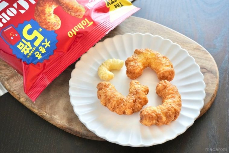 木のカッティングボードと白い皿にのったキャラメルコーングランデと赤い袋のパッケージとストライプの布