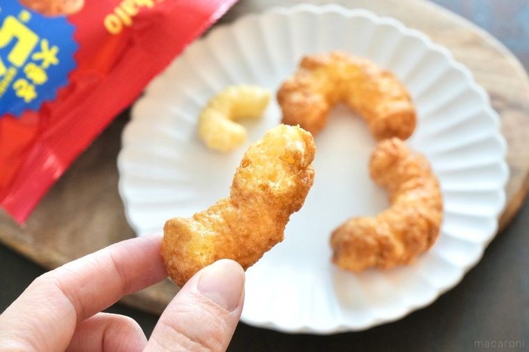 木のカッティングボードと白い皿にのったキャラメルコーングランデを持つ手と赤い袋のパッケージ