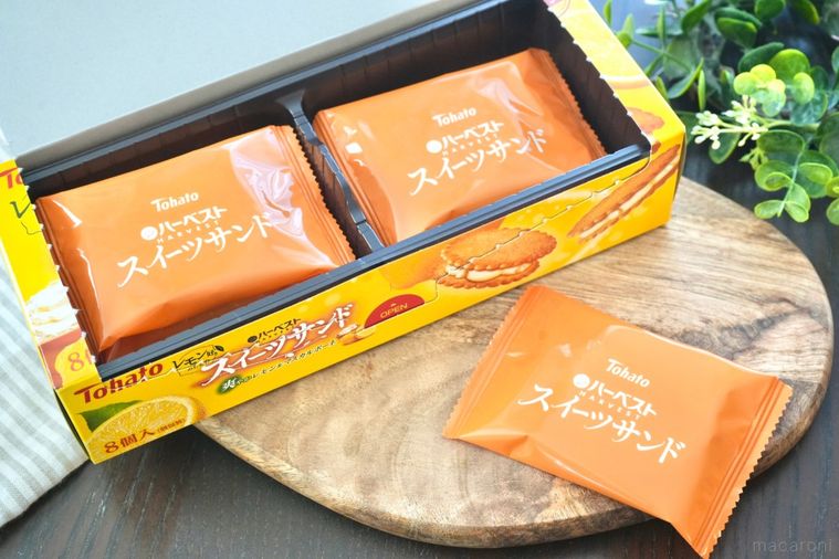 木のカッティングボードにのった黄色い箱のビスケットサンドとストライプの布とグリーン