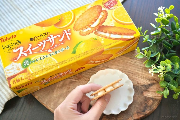 木のカッティングボードと白い皿にのったレモン味のビスケットサンドを手に持つ様子と黄色い箱のパッケージ